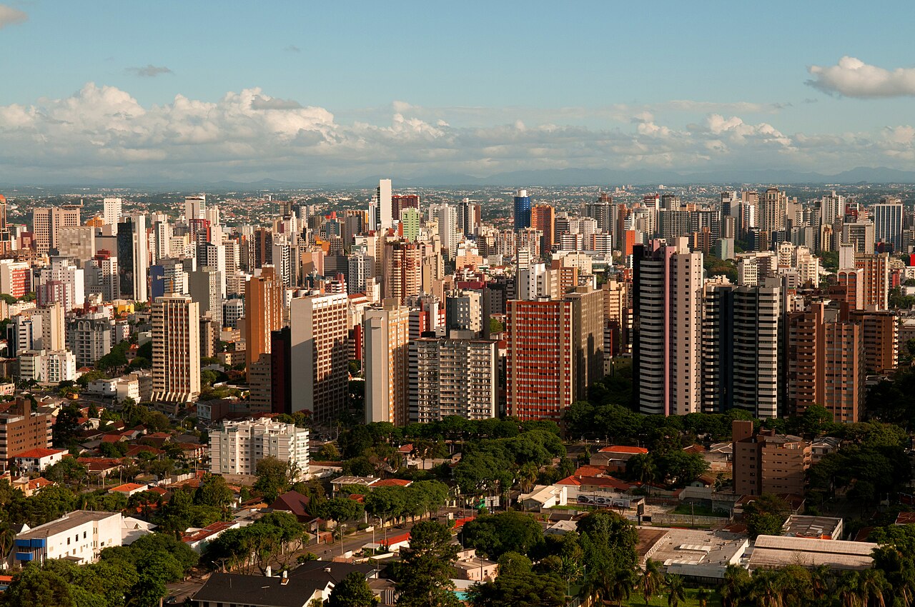 Vista panorâmica de Curitiba, Paraná, a partir da Torre Panorâmica, com prédios residenciais e áreas arborizadas sob céu com nuvens